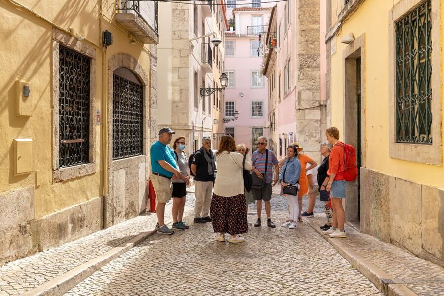 A guided group climbing a narrow lane of tiled houses in Lisbon